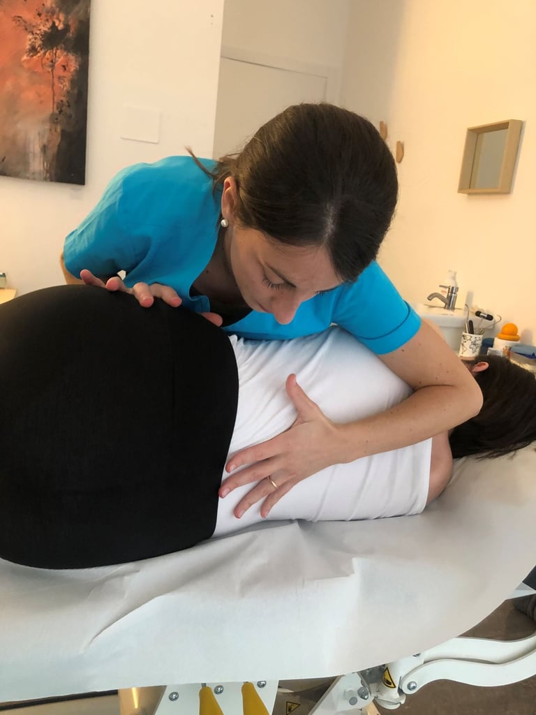 Healthcare provider in blue scrubs performing a back massage or spinal examination on a patient lying face down on a treatment table