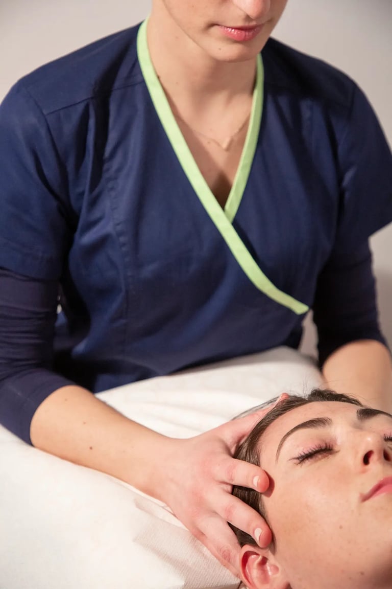 Professionista in camice blu navy con dettaglio lime che esegue un massaggio al viso su una paziente rilassata